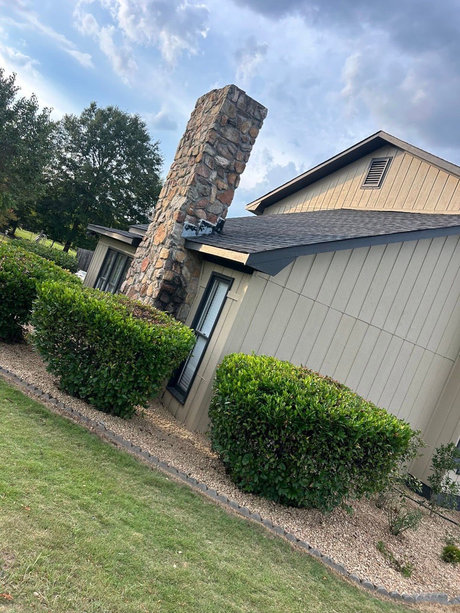 Shaped shrubs and rock landscape beds beside a stone chimney