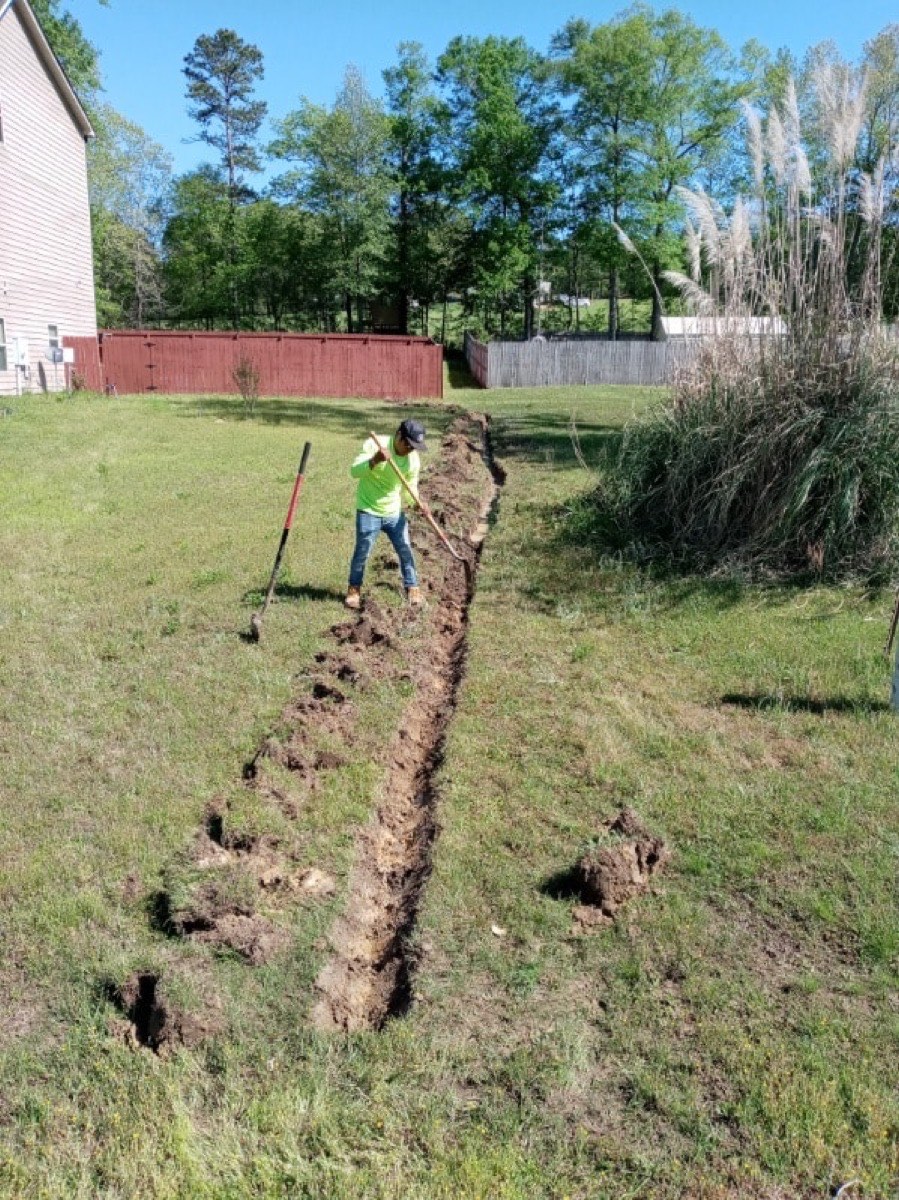 Crew member digging a trench line across a lawn